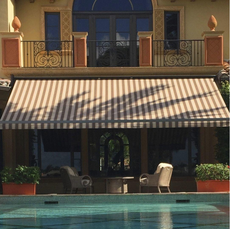 Maison en pierre avec piscine équipée d’un store banne rayé modèle Orchestra, coffre monobloc motorisé, toile acrylique Dickson, structure aluminium résistante offrant une protection solaire efficace